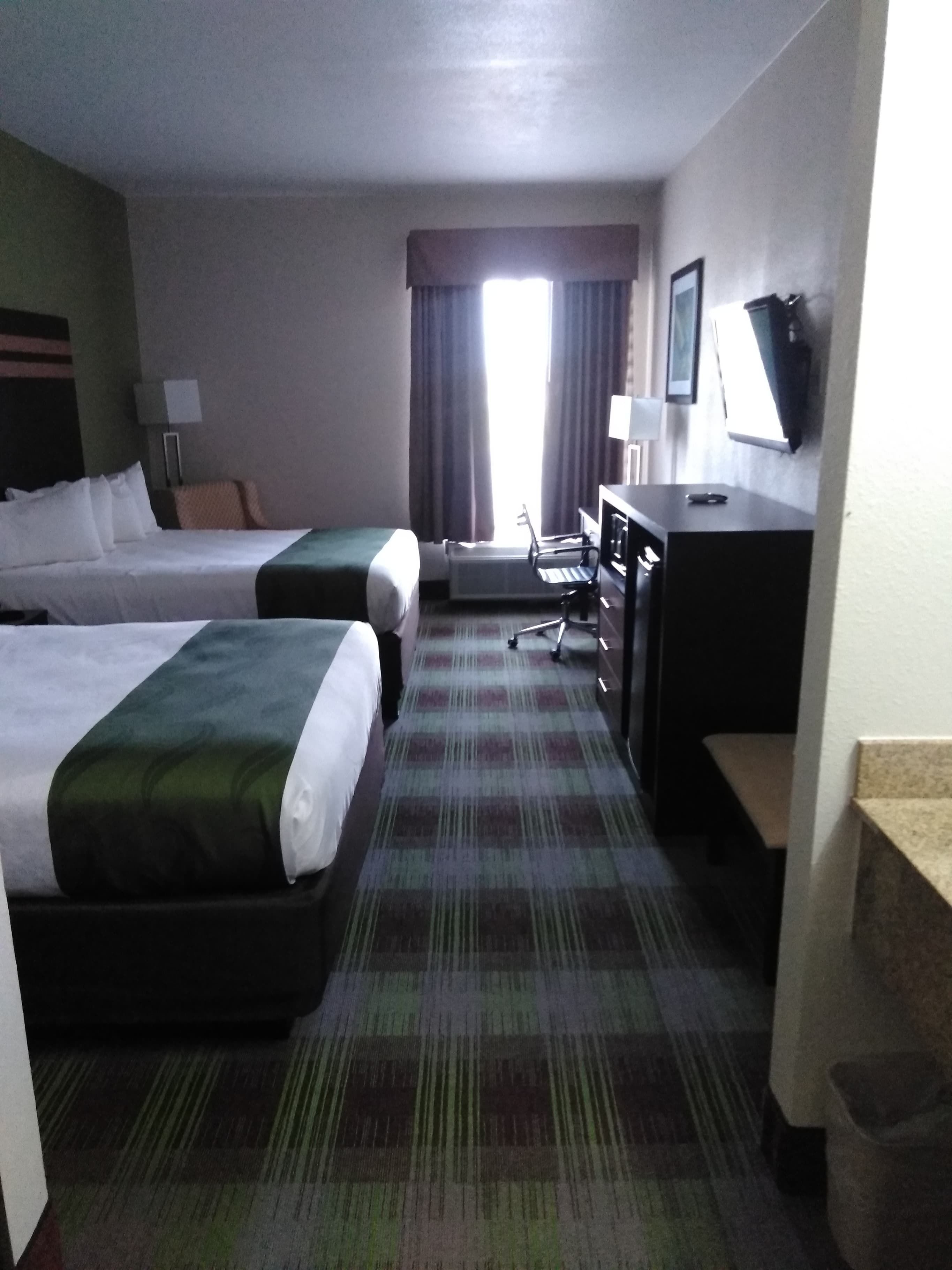 A hotel room with two beds, a desk, a chair, a TV, and a window with curtains.
