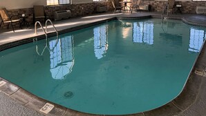 Una piscina interior con agua cristalina, un letrero de salvavidas y una pared de piedra.