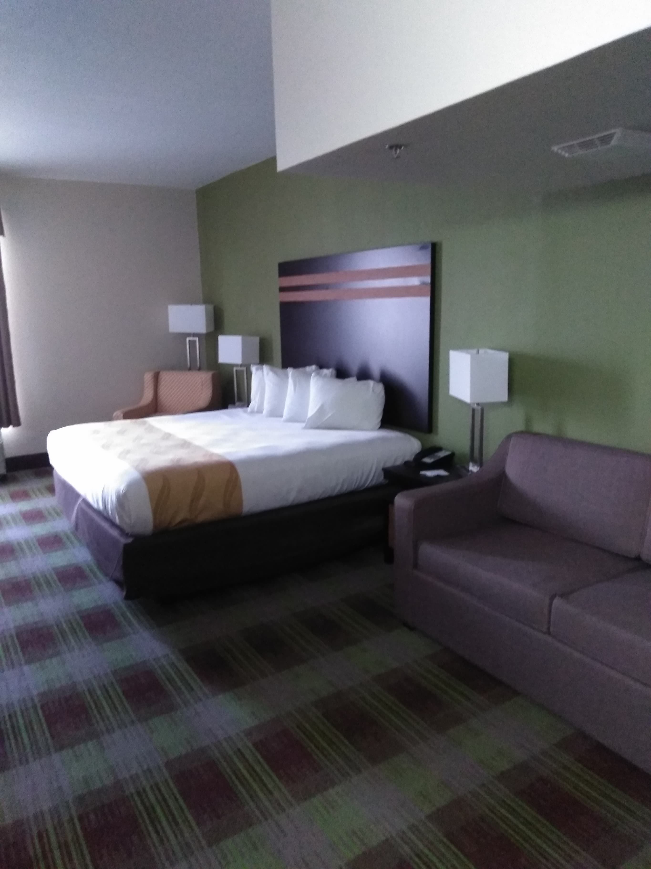 A hotel room with a bed, a sofa, two bedside tables with lamps, and a large abstract painting on the wall.