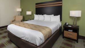 Habitación de hotel con una cama grande, dos lámparas de noche, una silla, una mesita de noche con un teléfono y una obra de arte en la pared.