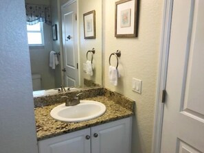 A bathroom with a granite countertop sink, white cabinets, and two framed pictures on the wall. - Club Bamboo South (Bradenton Beach)