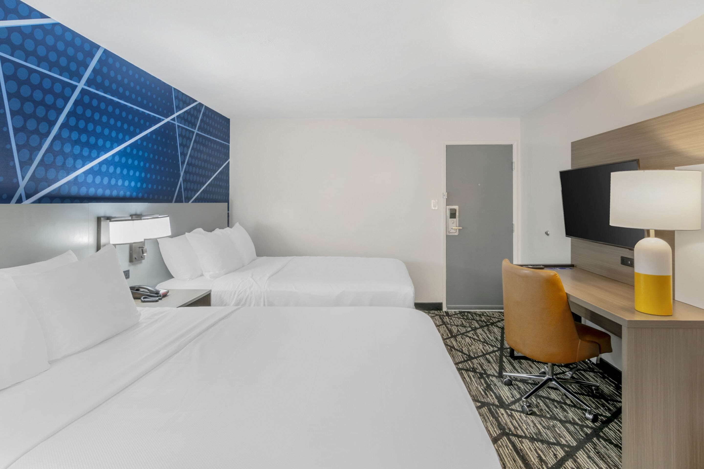 Una habitación de hotel con dos camas, un escritorio con lámpara, un televisor y una alfombra estampada.