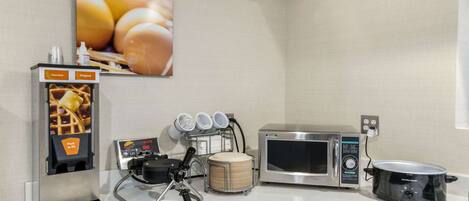 Una kitchenette equipada con un fabricante de gofres, un microondas, una olla de cocción lenta y un dispensador de gofres.