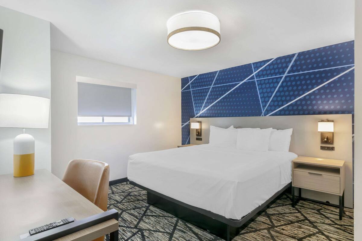 A hotel room with a bed, bedside tables, a desk with a lamp, and a patterned carpet.