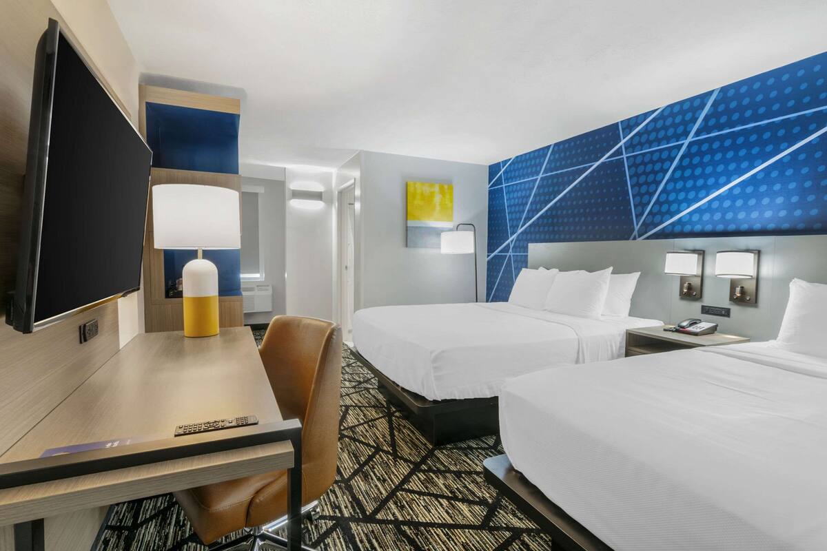 A hotel room with two beds, a desk with a TV, a lamp, and a chair.