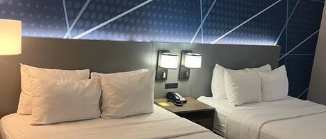 Habitación de hotel con dos camas, una mesita de noche con teléfono y techo con estampado geométrico.