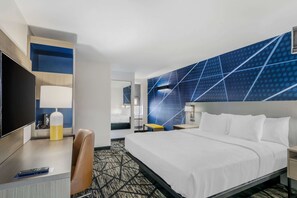 A hotel room with a bed, a desk with a chair, a TV, and a wall with a geometric pattern. - Comfort Inn Kansas City Midtown (Kansas City)