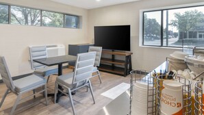 A modern dining area with a large flat-screen TV, a buffet setup, and a view of the street through large windows. - Comfort Inn Kansas City Midtown (Kansas City)