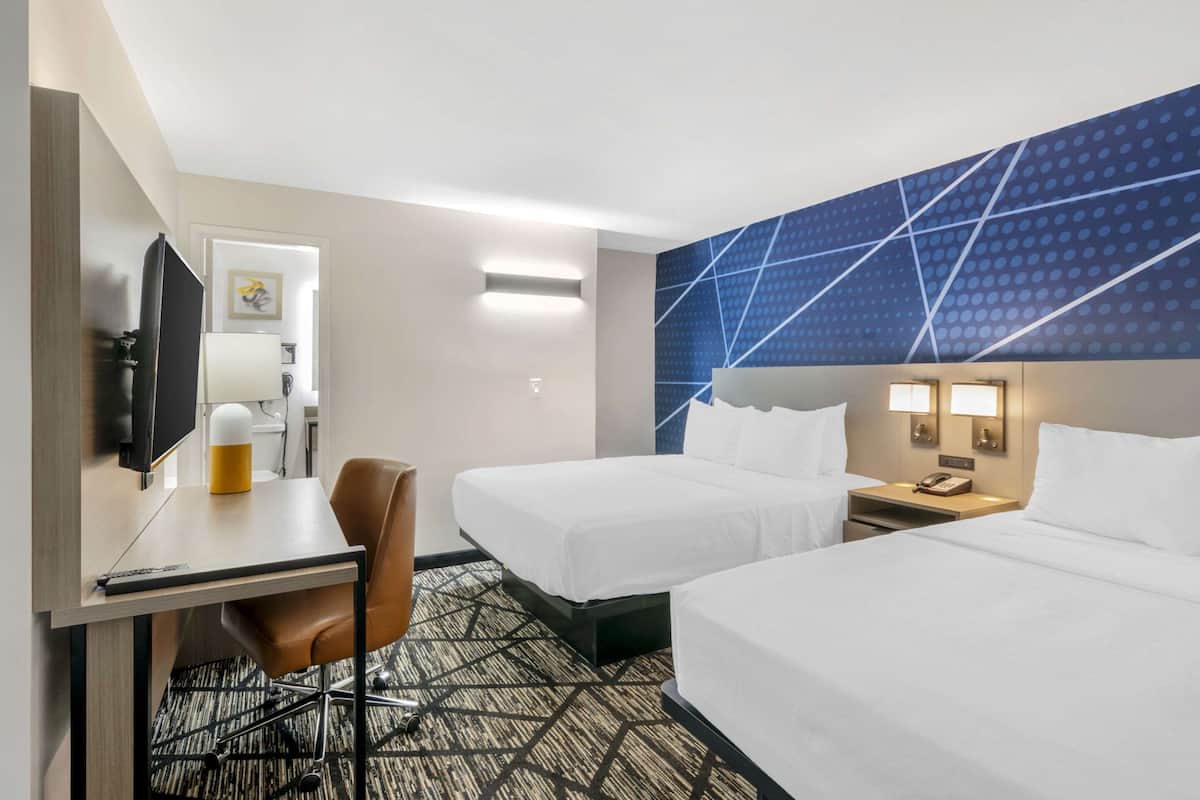 A hotel room with two beds, a desk with a chair, a television, and a wall-mounted phone.