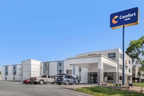 A Comfort Inn hotel with a modern design, featuring a parking lot with several vehicles and a clear blue sky. - Comfort Inn Kansas City Midtown (Kansas City)