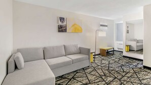 A modern hotel room with a grey sofa, a patterned carpet, and artwork on the wall. - Comfort Inn Kansas City Midtown (Kansas City)