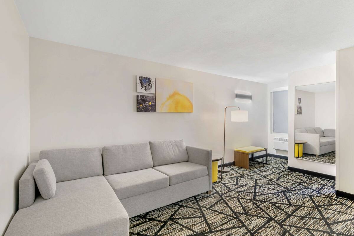 A modern hotel room with a grey sofa, a patterned carpet, and artwork on the wall.