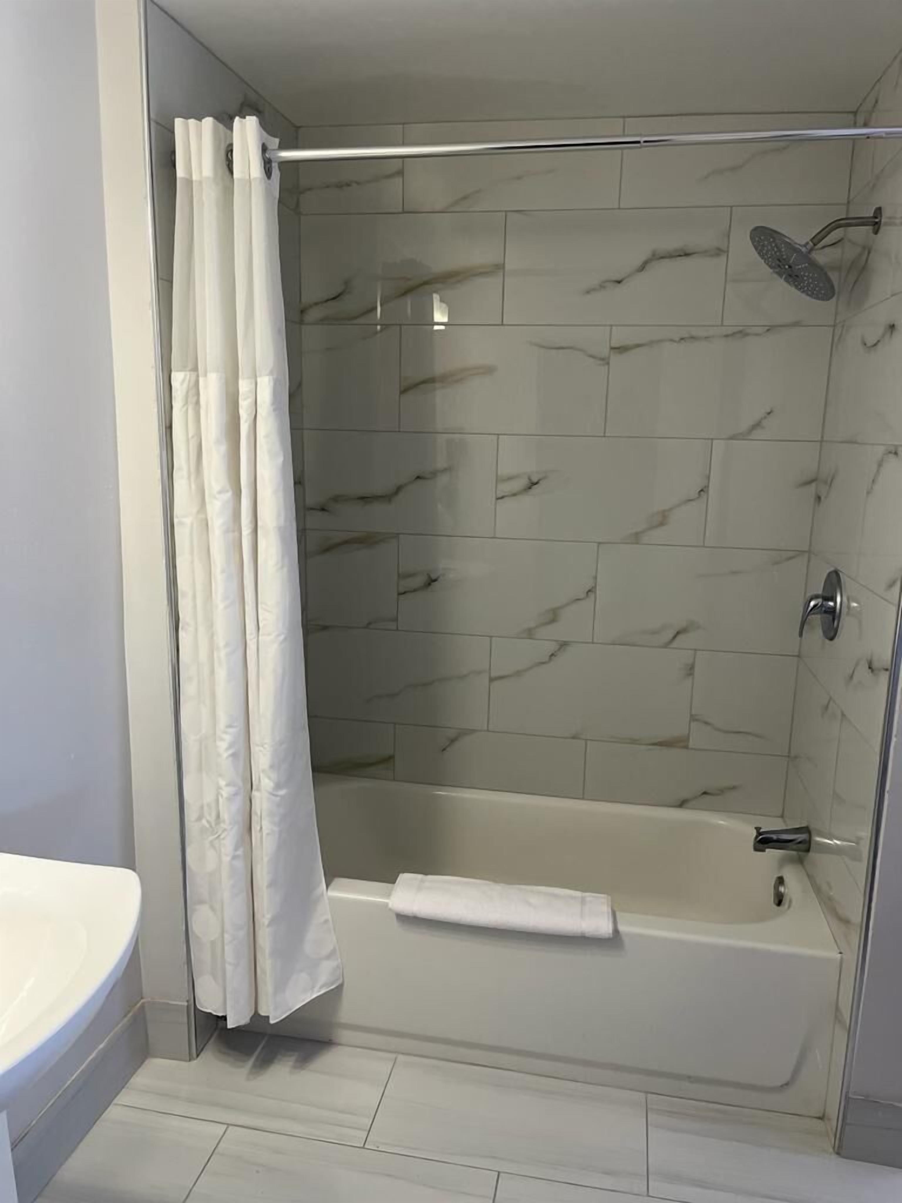 Uma casa de banho moderna com chuveiro em cabine de vidro, uma banheira branca e uma sanita.