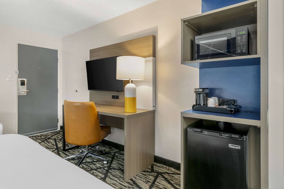 A hotel room with a bed, a desk with a lamp, a television, a microwave, and a mini-fridge.