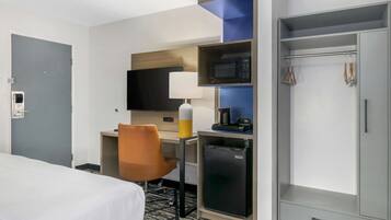 A hotel room with a bed, a desk with a chair, a microwave, a mini-fridge, a wardrobe, and a television.