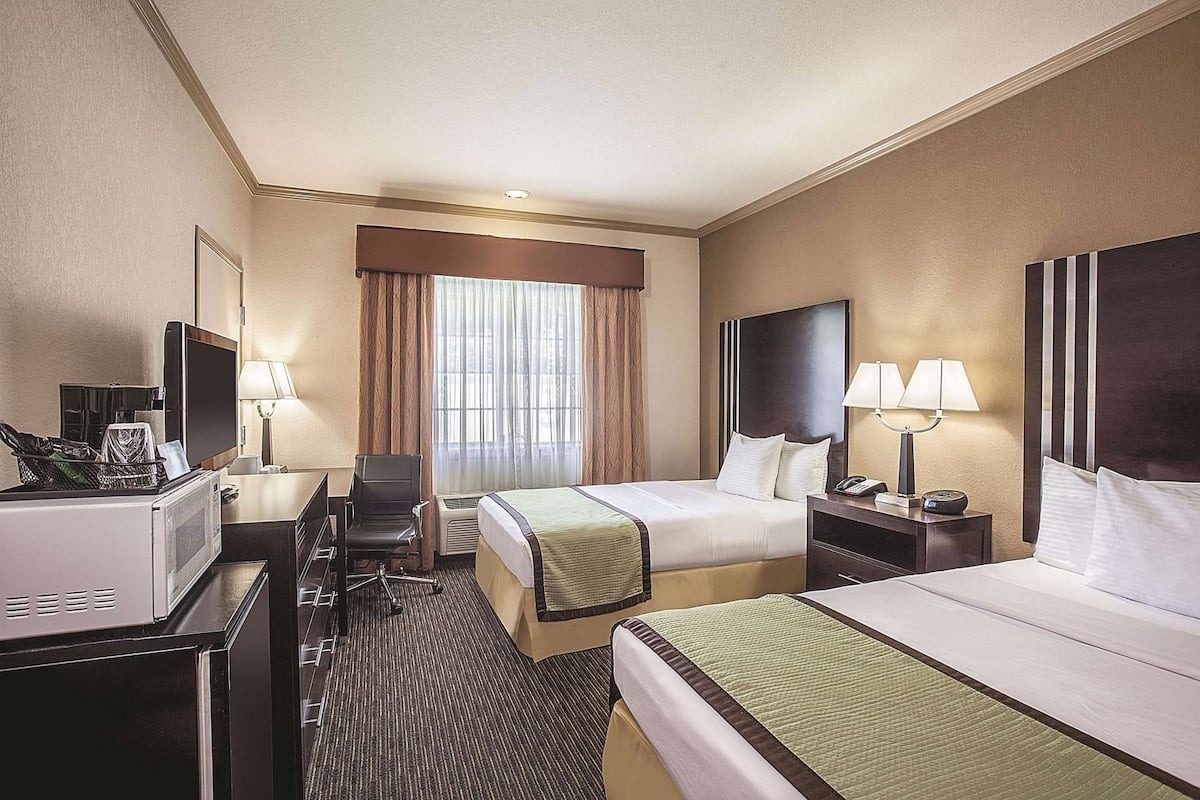 A hotel room with two beds, a desk, a TV, and a window with curtains.