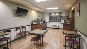 A restaurant with wooden tables and chairs, a flat-screen TV mounted on the wall, and a kitchen area visible through the window. - La Quinta Inn & Suites by Wyndham Davis (Davis)