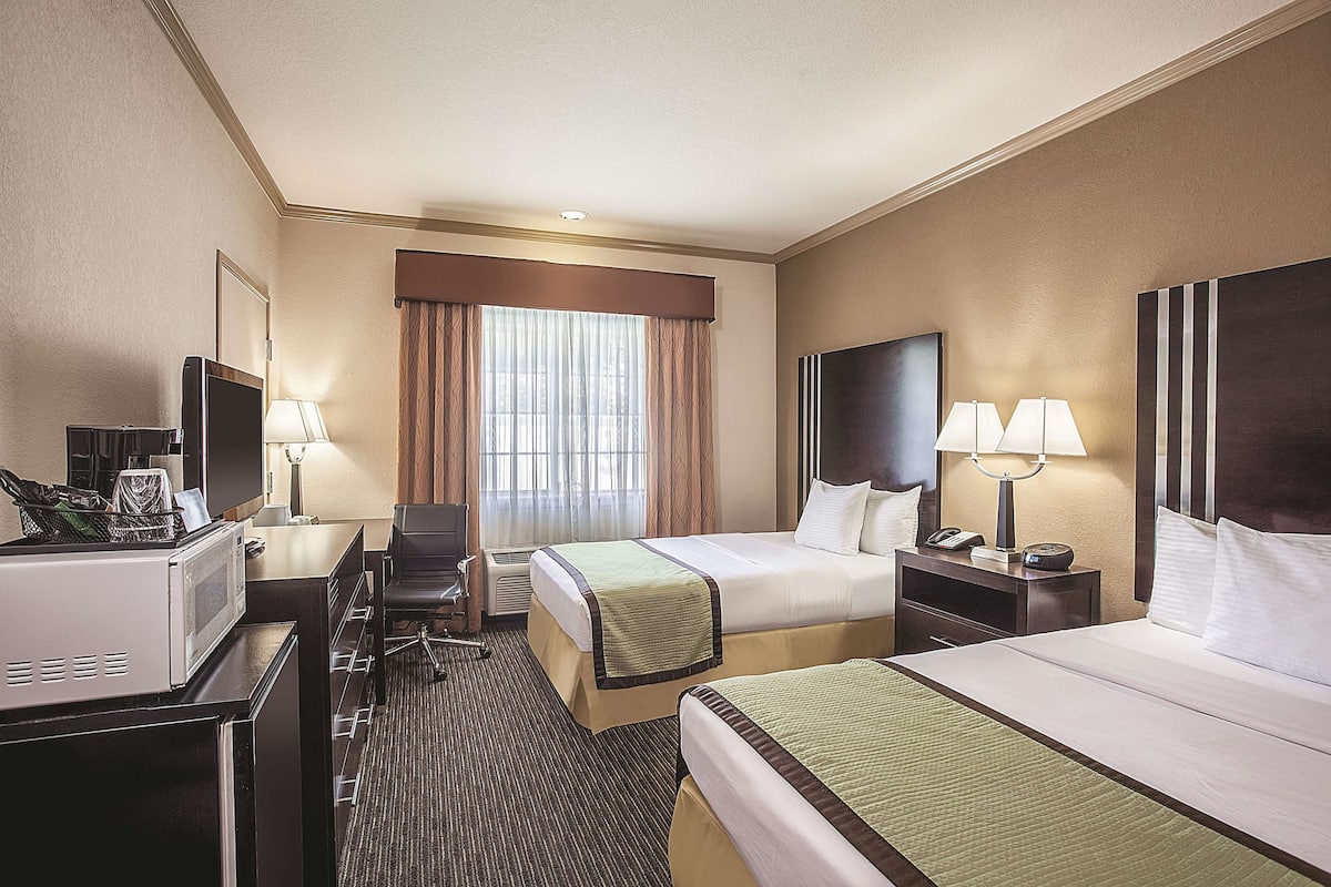 A hotel room with two beds, a desk with a computer, a TV, and a minibar.