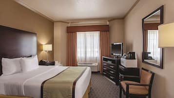 A hotel room with a large bed, a desk with a computer, a TV, and a chair.