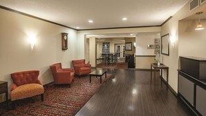 A spacious hotel lobby with a red patterned carpet, a seating area with two armchairs and a sofa, a small table, and a television on a stand. - La Quinta Inn & Suites by Wyndham Davis (Davis)