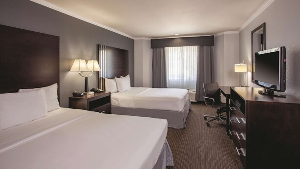 A hotel room with two beds, a desk, a chair, a TV, and a window with curtains. - La Quinta Inn & Suites by Wyndham Davis (Davis)