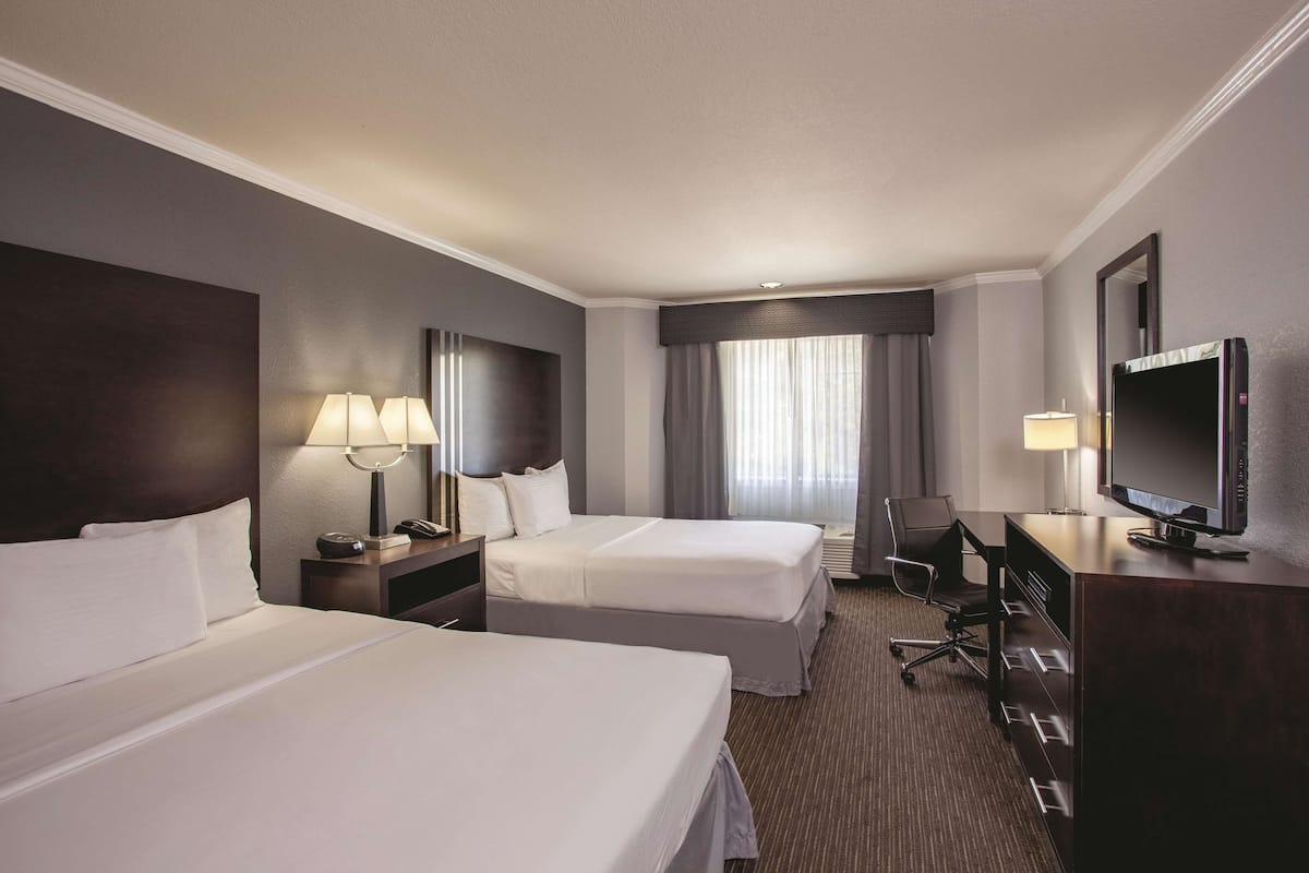 A hotel room with two beds, a desk, a chair, a TV, and a window with curtains.