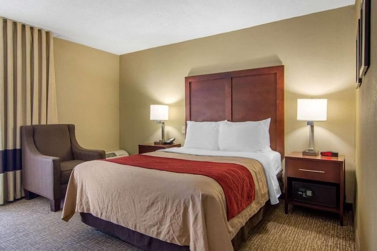 A hotel room with a large bed, two bedside tables with lamps, a chair, and a window with curtains.