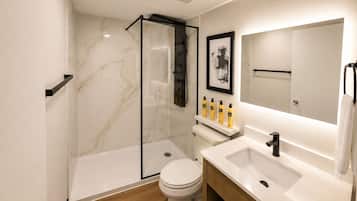 A modern bathroom with a glass shower enclosure, a toilet, a sink with a mirror, and a shelf with toiletries.