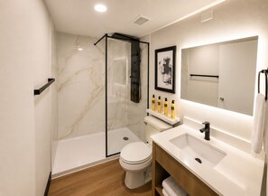 A modern bathroom with a glass shower enclosure, a toilet, a sink with a mirror, and a shelf with toiletries.