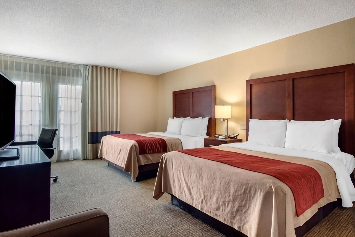 A hotel room with two beds, a desk, and a television.