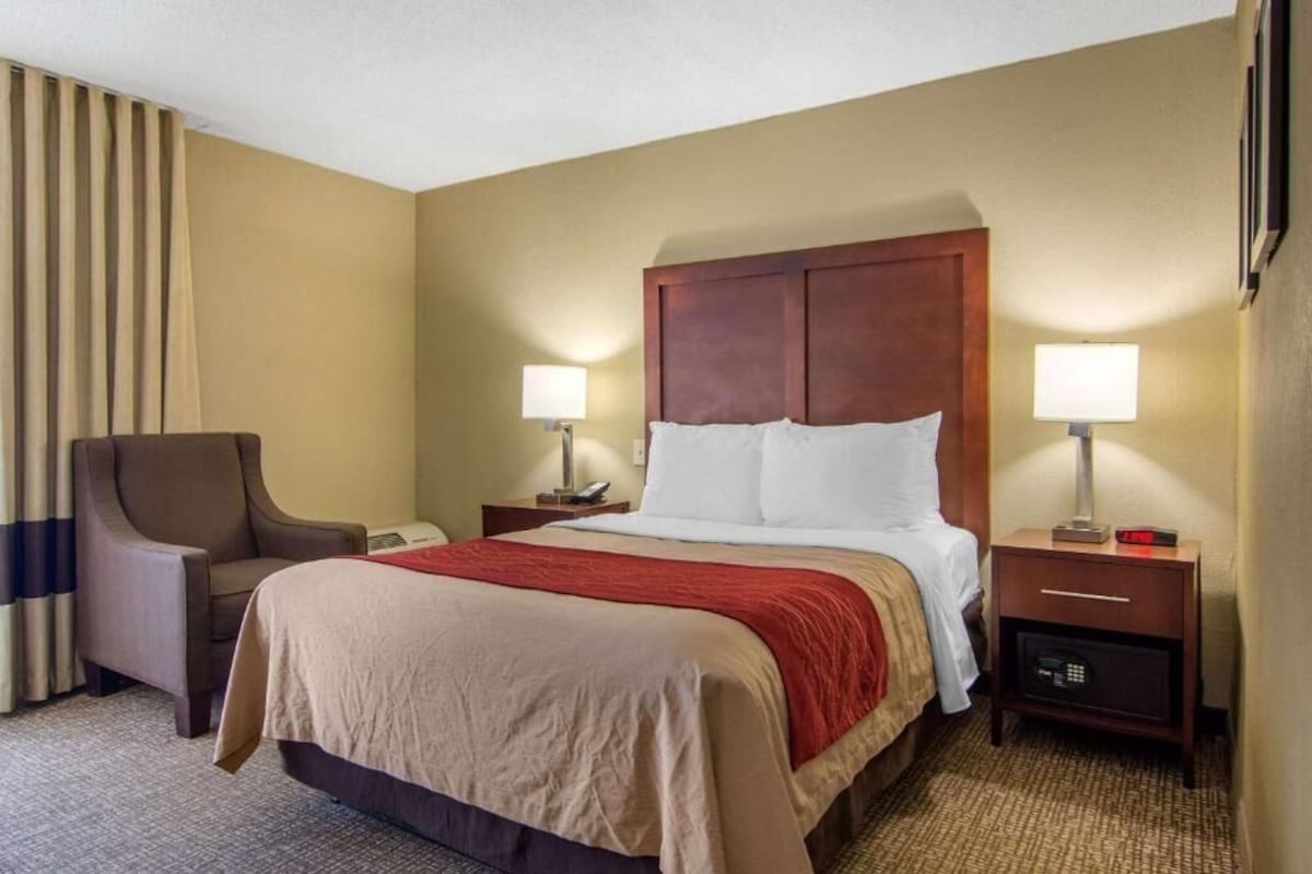 A hotel room with a bed, two bedside tables, a chair, a lamp, and a window with curtains.