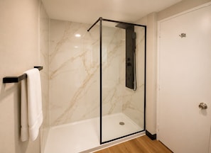 A glass-enclosed shower with a control panel, a white towel on a black towel rack, and a door with a silver handle. - Best Western Plus Atlanta Sandy Springs Perimeter Hotel (Atlanta)