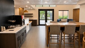 A modern dining area with a wooden table and chairs, a kitchen counter with appliances, and a view through the glass door. - Best Western Plus Atlanta Sandy Springs Perimeter Hotel (Atlanta)