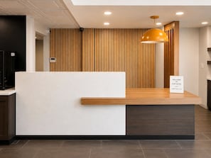 A hotel reception desk with a wooden panel backdrop, a 'Welcome to Our Hotel' sign, and a modern pendant light. - Best Western Plus Atlanta Sandy Springs Perimeter Hotel (Atlanta)