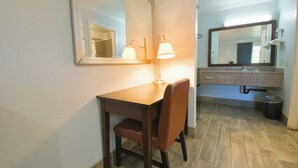 A hotel room with a wooden desk, a chair, a large mirror, and a bathroom with a sink and mirror. - Welcome Inn (Corona)