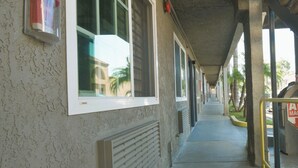 A covered walkway with windows, a fire alarm, and a building exterior. - Welcome Inn (Corona)