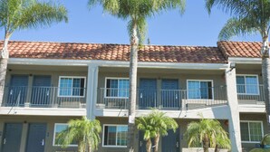 A multi-story building with a red-tiled roof, balconies, and palm trees in front. - Welcome Inn (Corona)