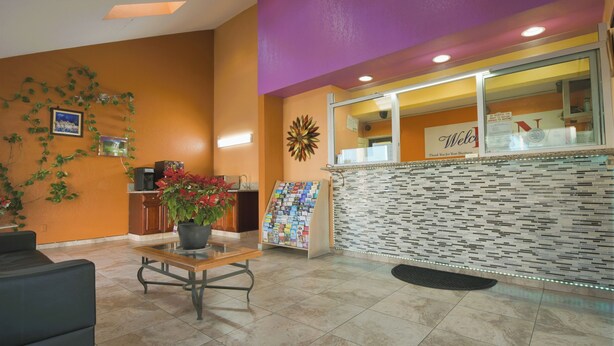 A reception area with a counter, a welcome sign, a magazine rack, and a potted plant. - Welcome Inn (Corona)