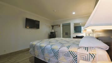 Habitación de hotel con cama, televisor montado en la pared, lámpara de noche, teléfono y espejo sobre la cama.