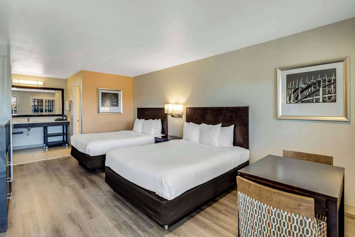 A hotel room with two beds, a desk, and a chair.