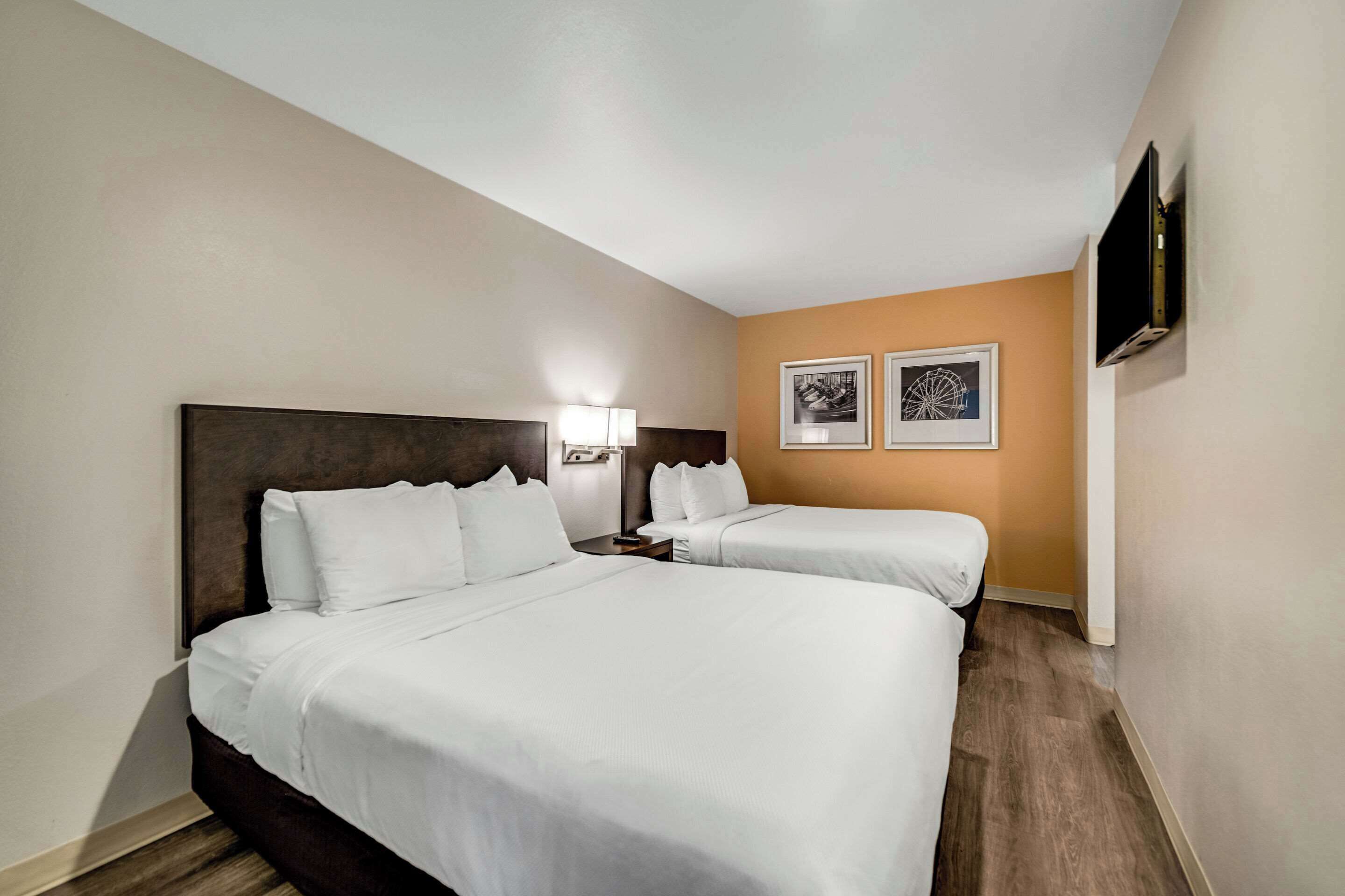 Une chambre d’hôtel avec deux lits, un téléviseur fixé au mur et deux tableaux encadrés accrochés au mur.