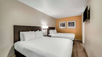 Une chambre d’hôtel avec deux lits, un téléviseur fixé au mur et deux tableaux encadrés accrochés au mur.