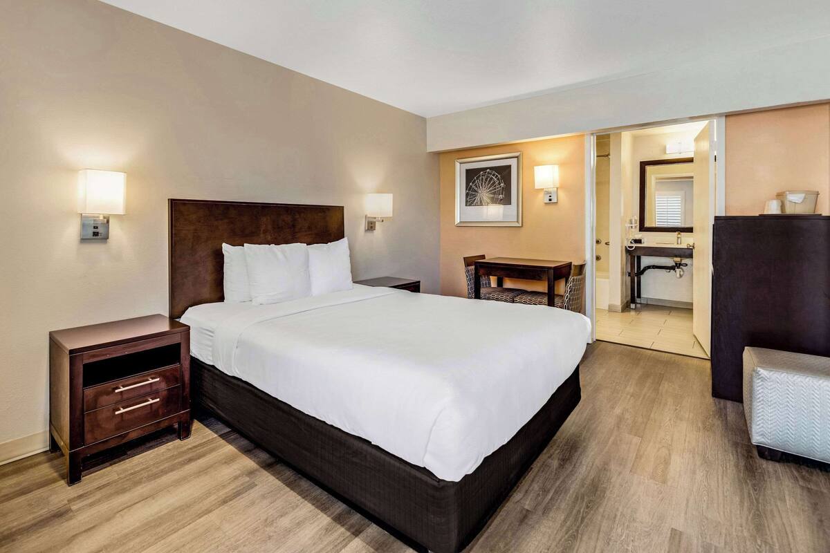 A hotel room with a large bed, bedside tables, a desk, and a bathroom visible through an open door.