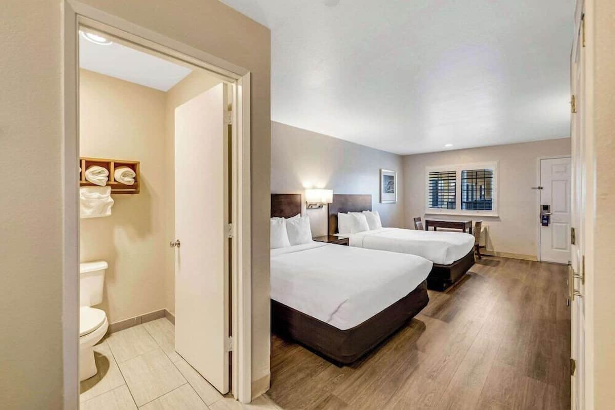 A hotel room with two beds, a bathroom, and a window with blinds.