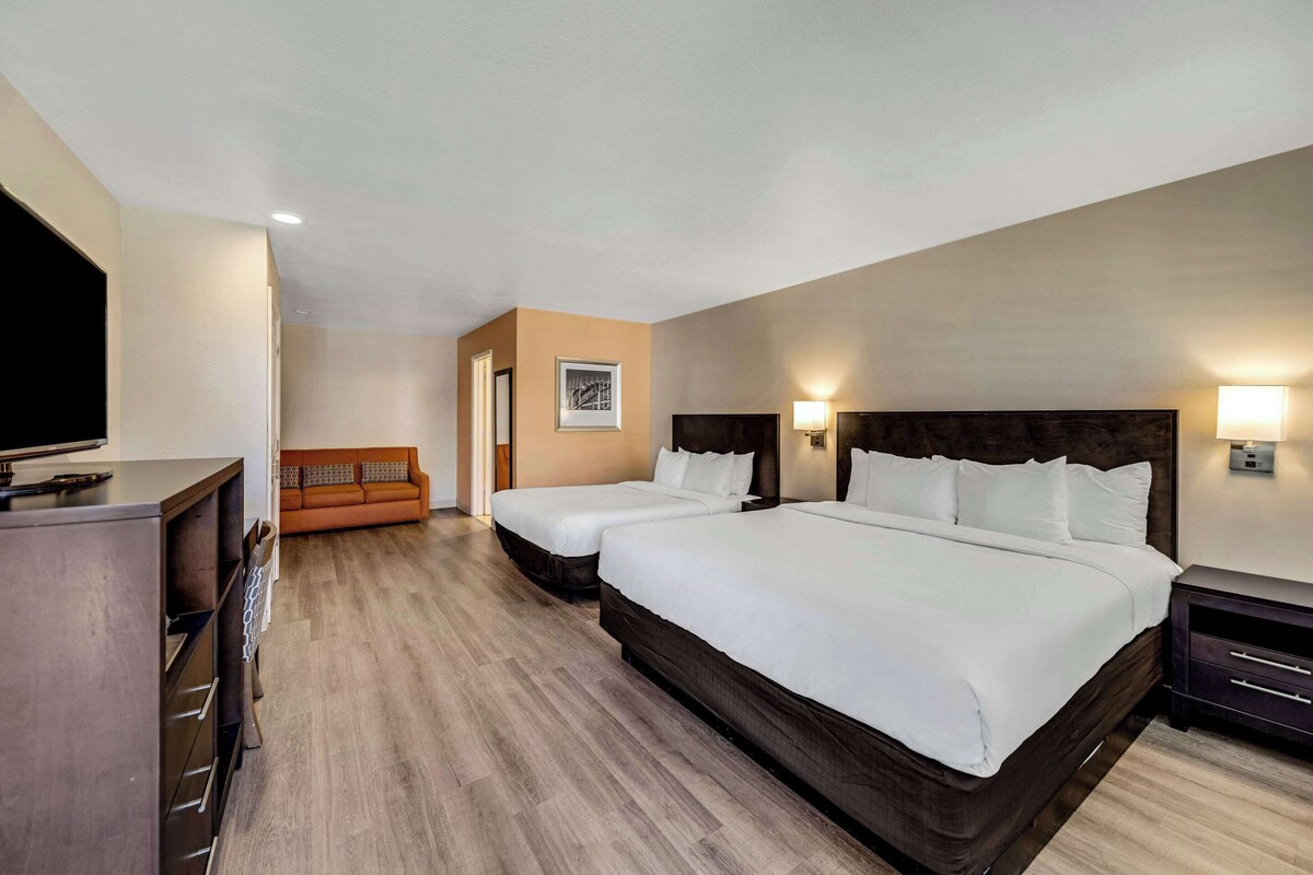 Quarto de hotel com duas camas, um sofá, uma televisão e uma secretária.