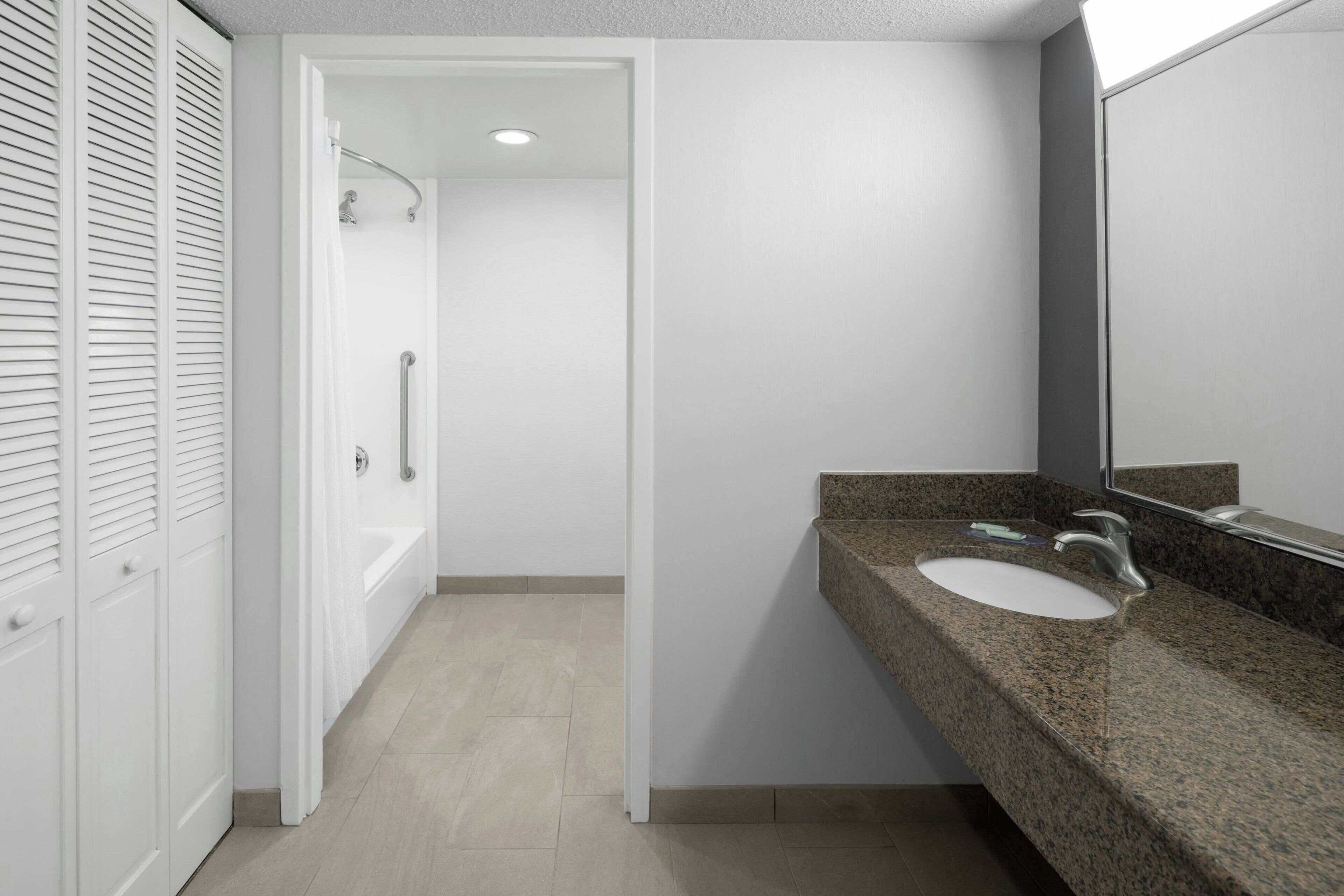 A modern bathroom with a granite countertop, a white sink, and a large mirror.