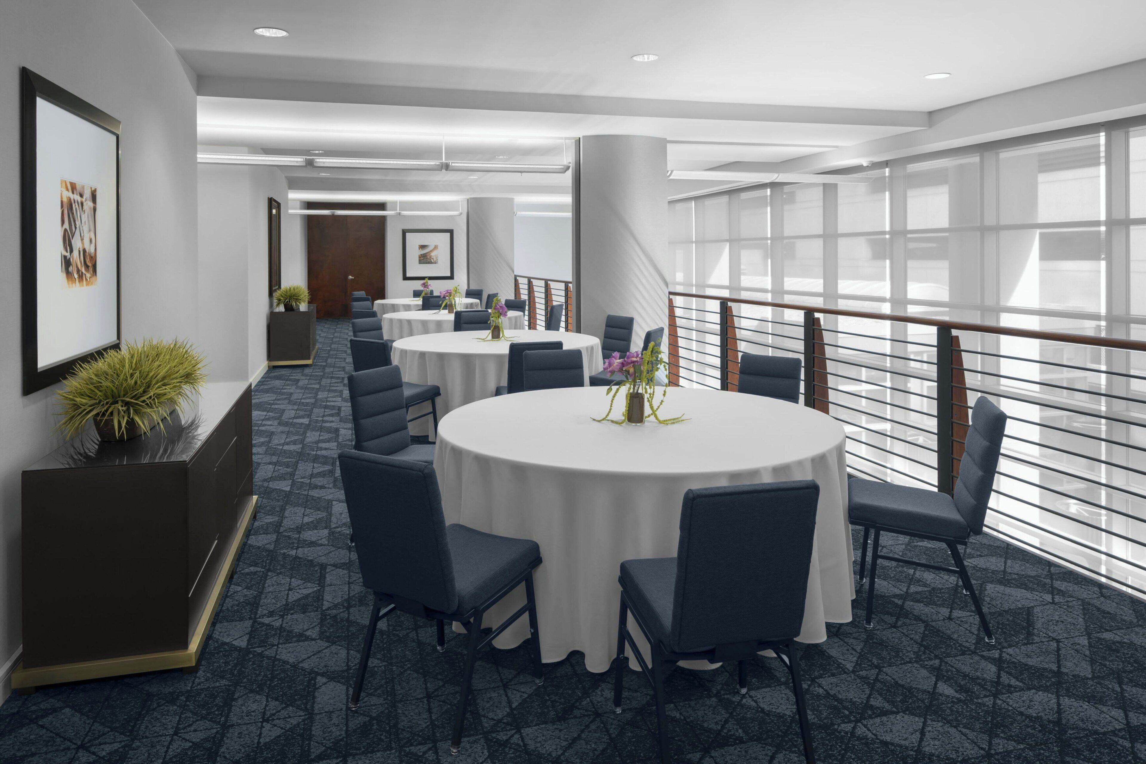 A modern conference room with round tables, dark chairs, and large windows.
