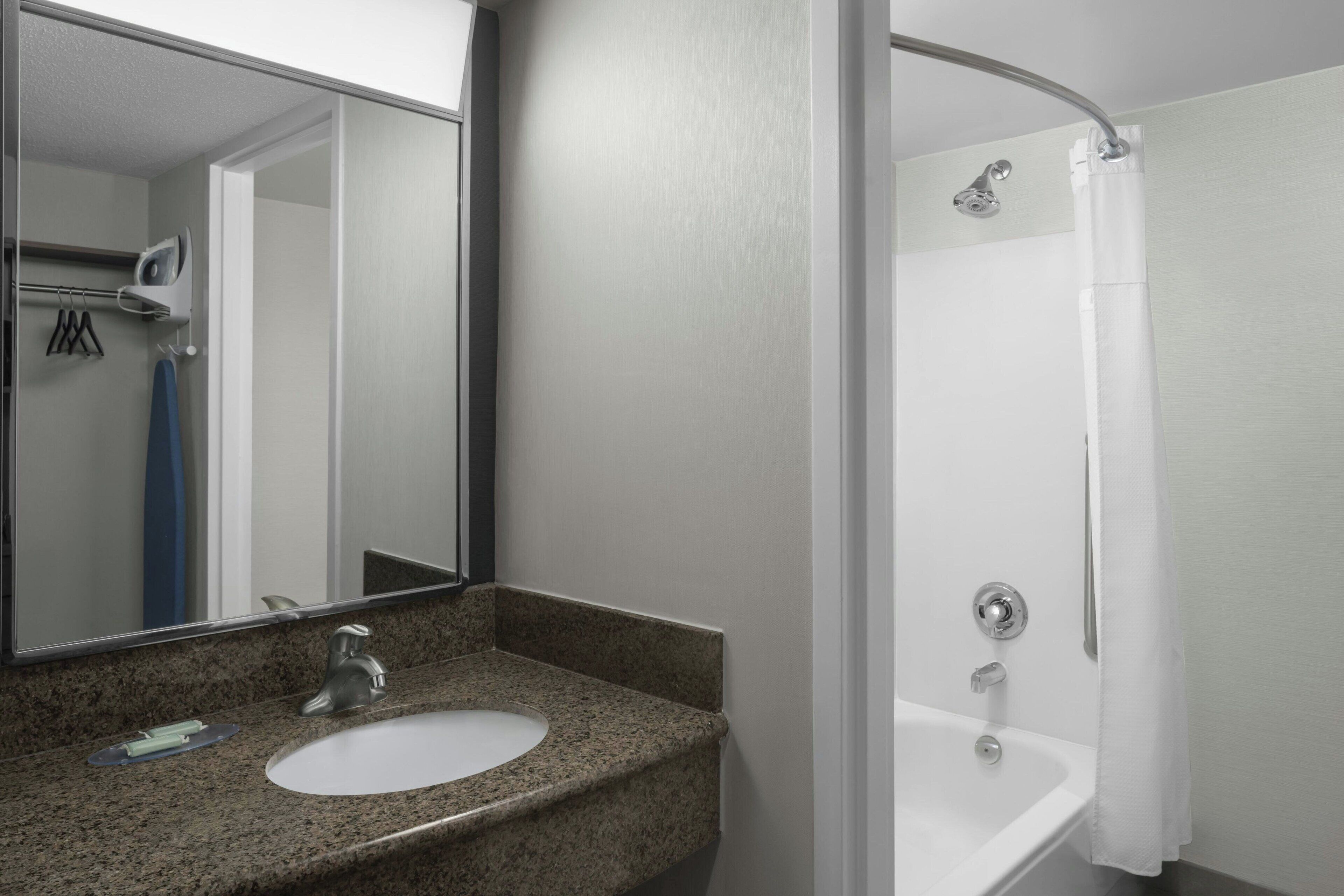 A bathroom with a granite countertop sink, a mirror, a shower with a white curtain, and a towel rack.