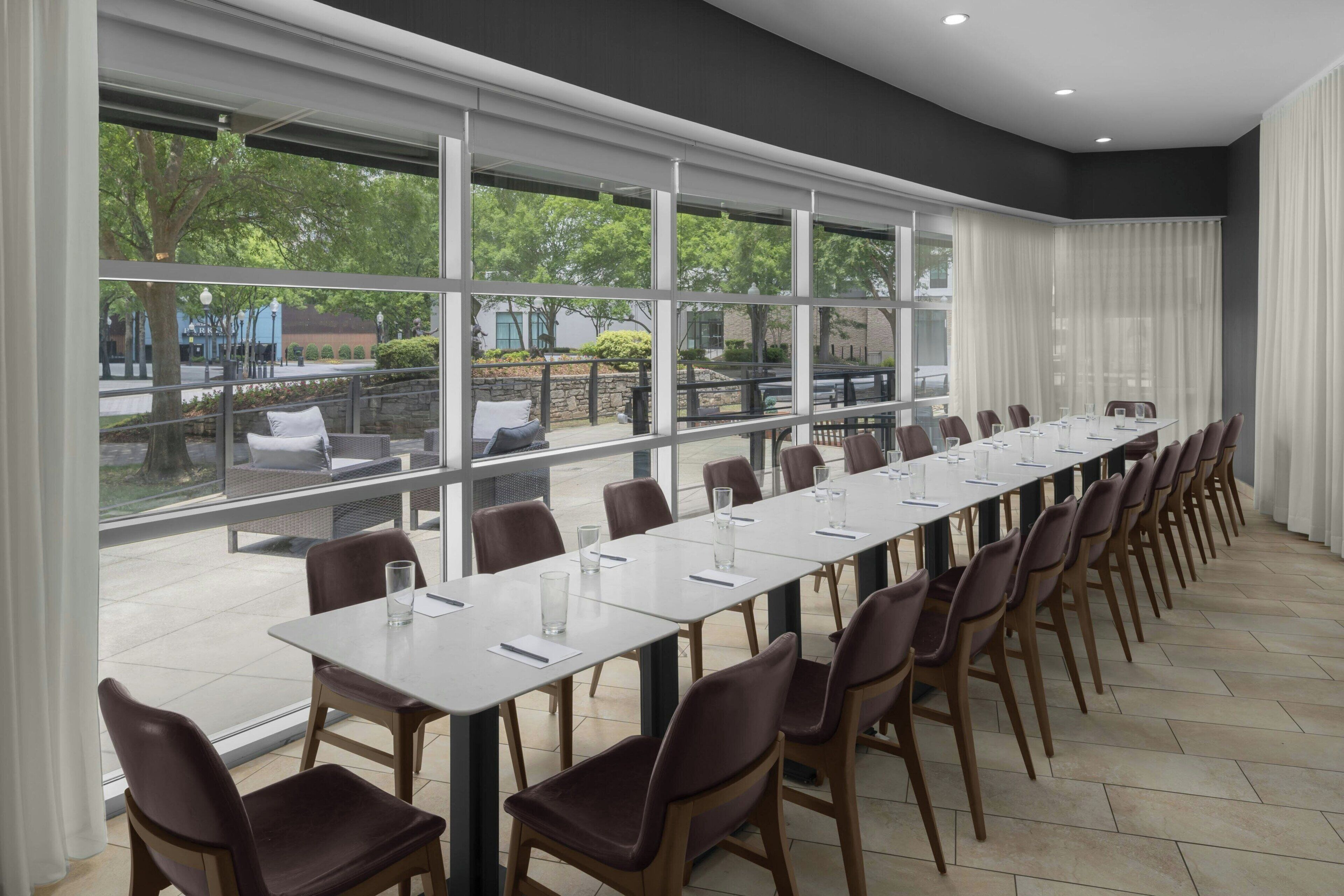 A conference room with a long table and chairs, large windows, and a view of the outdoors.