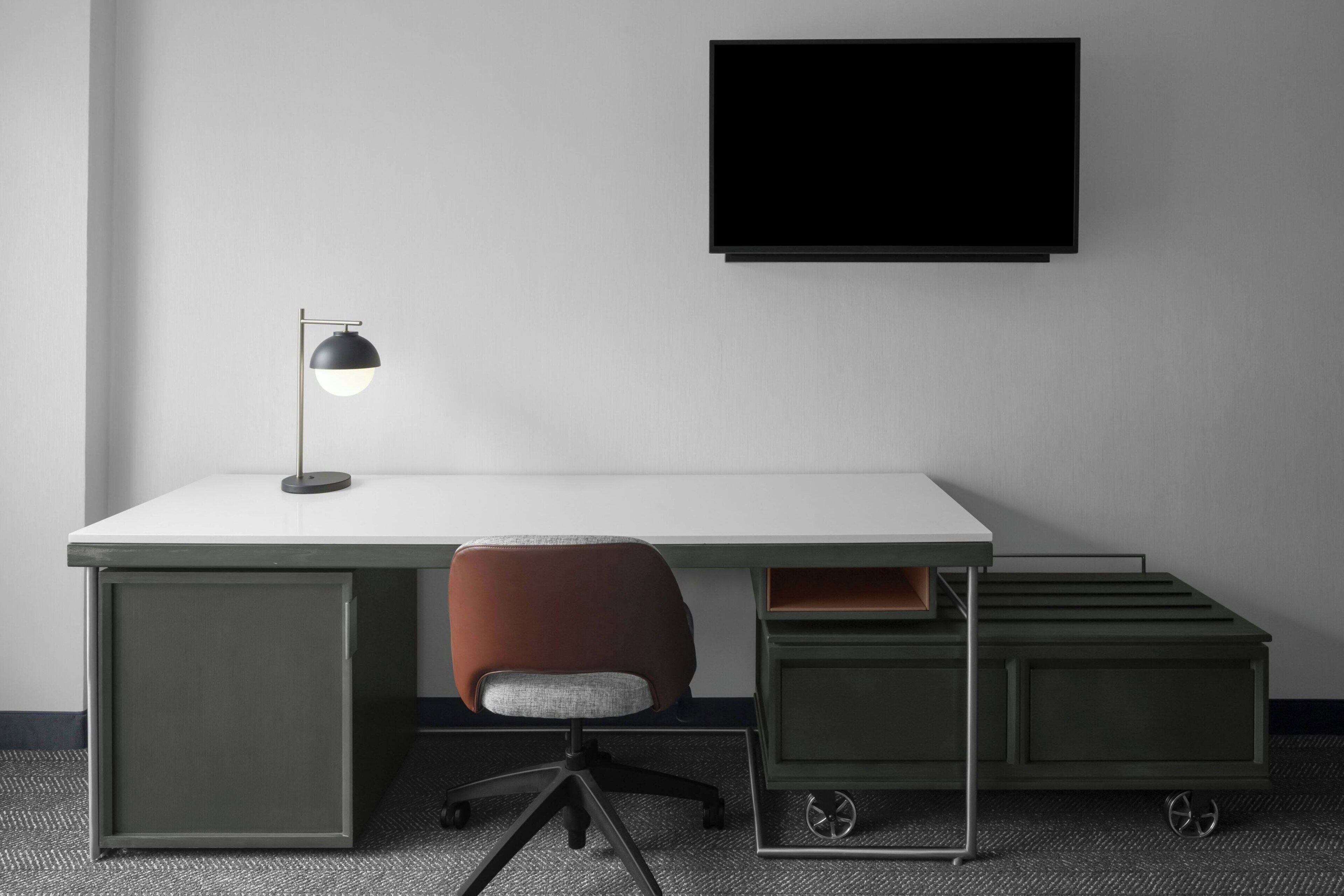 Un bureau moderne avec une chaise, une lampe de bureau et un téléviseur fixé au mur.